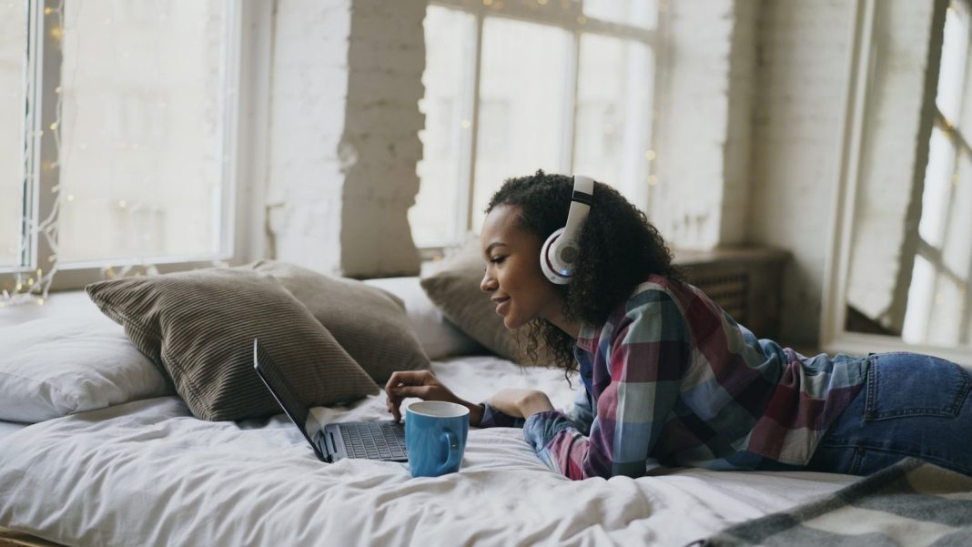 Young woman wearing headphones on bed with laptop.