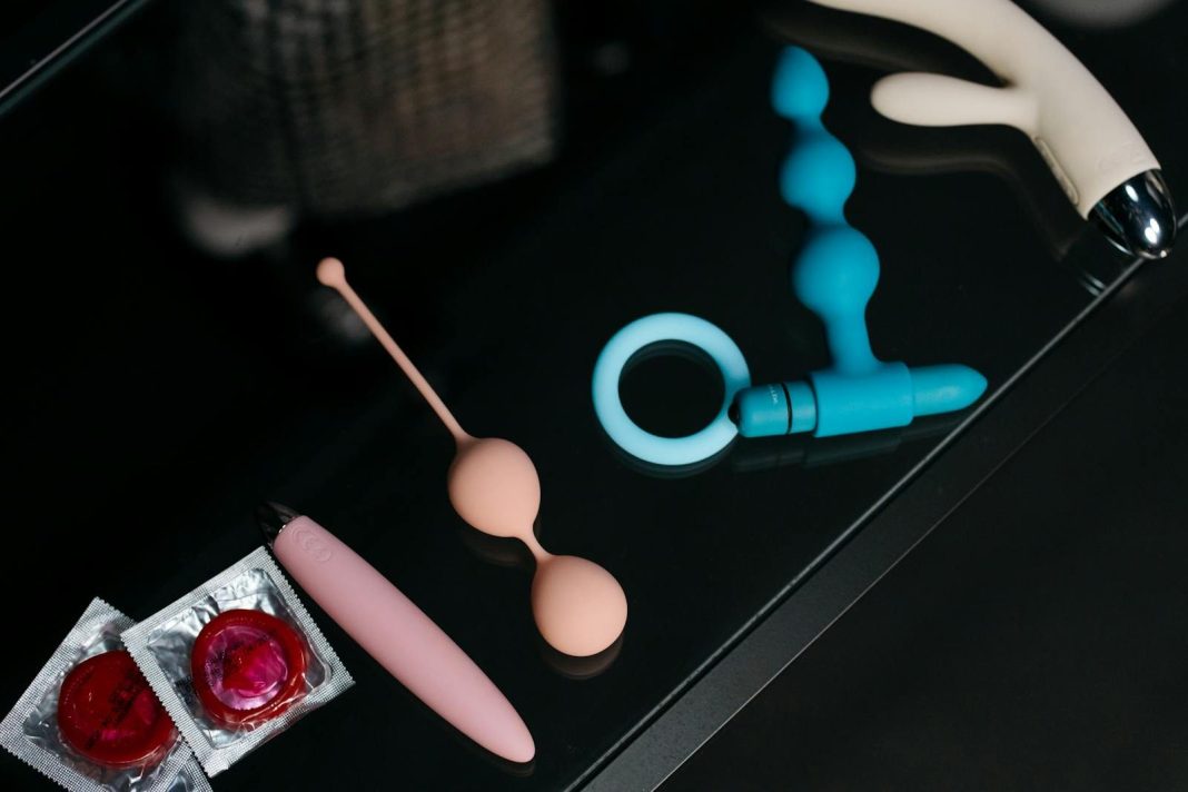 A collection of various sex toys and condoms on a reflective tabletop for safe and sensual pleasure.